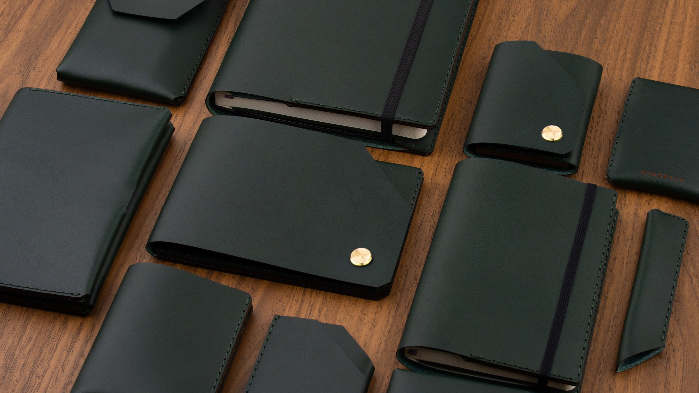 Wingback leather wallets and accessories in British Racing Green laid out on a walnut desk
