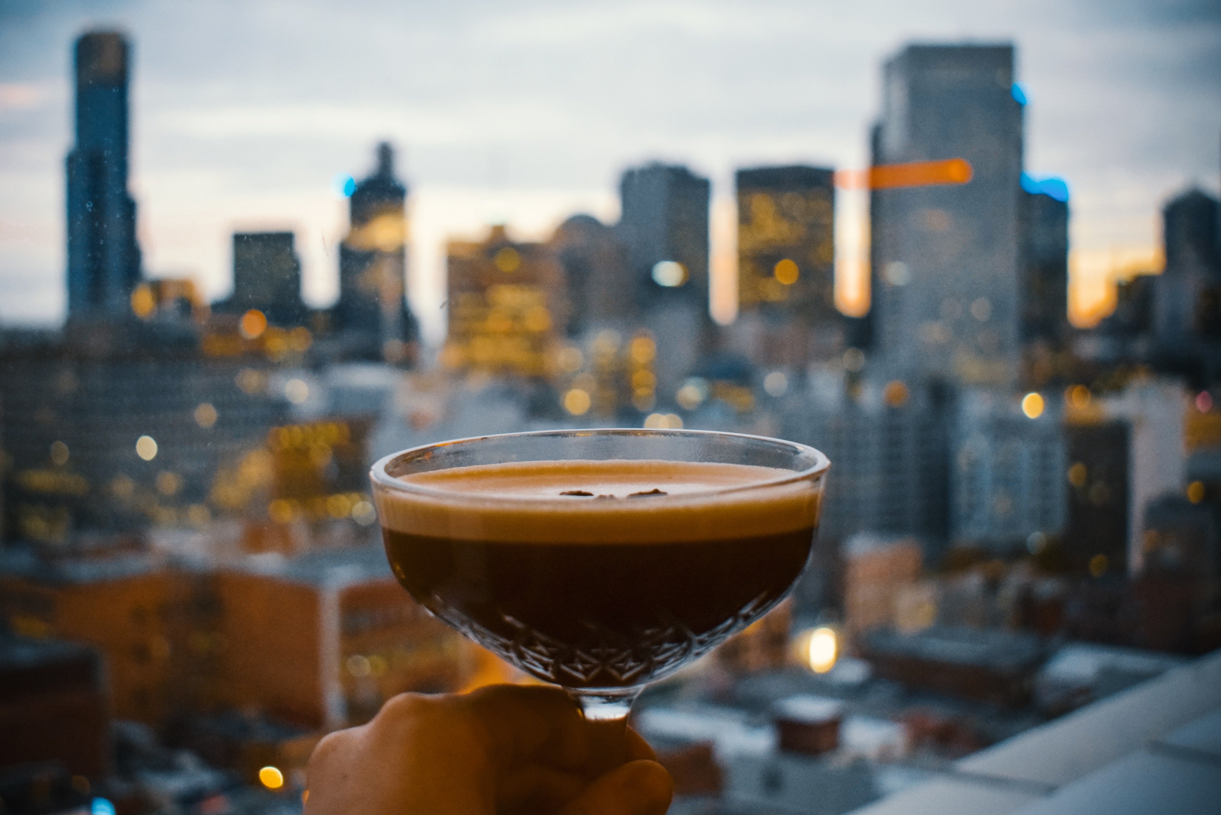 Espresso martini in foreground with a city scape in the background - Photo by Agathe on Unsplash