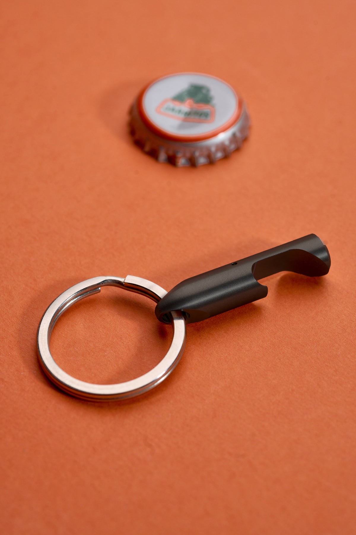 Bottle Opener - Black Steel on its key ring beside a lifted cap