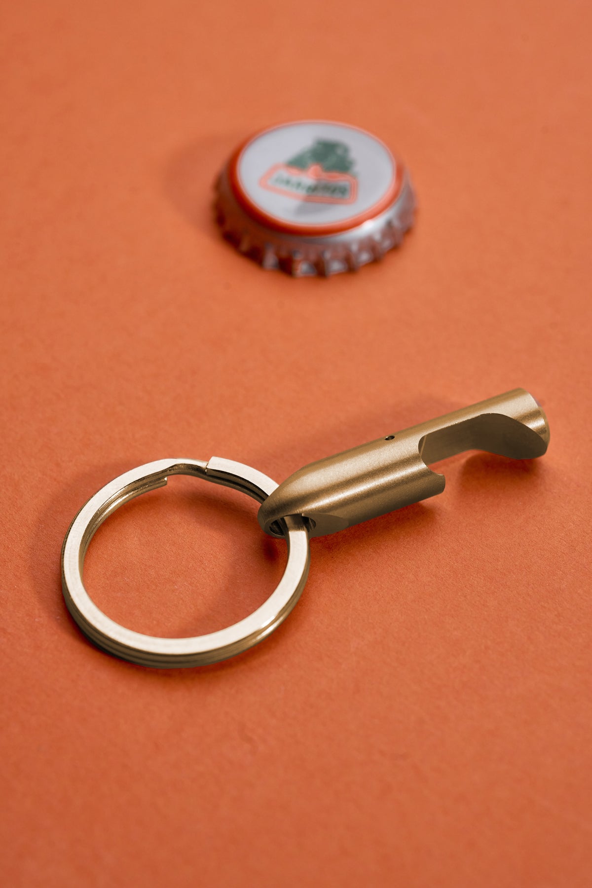 Bottle Opener - Brass on its key ring beside a lifted cap