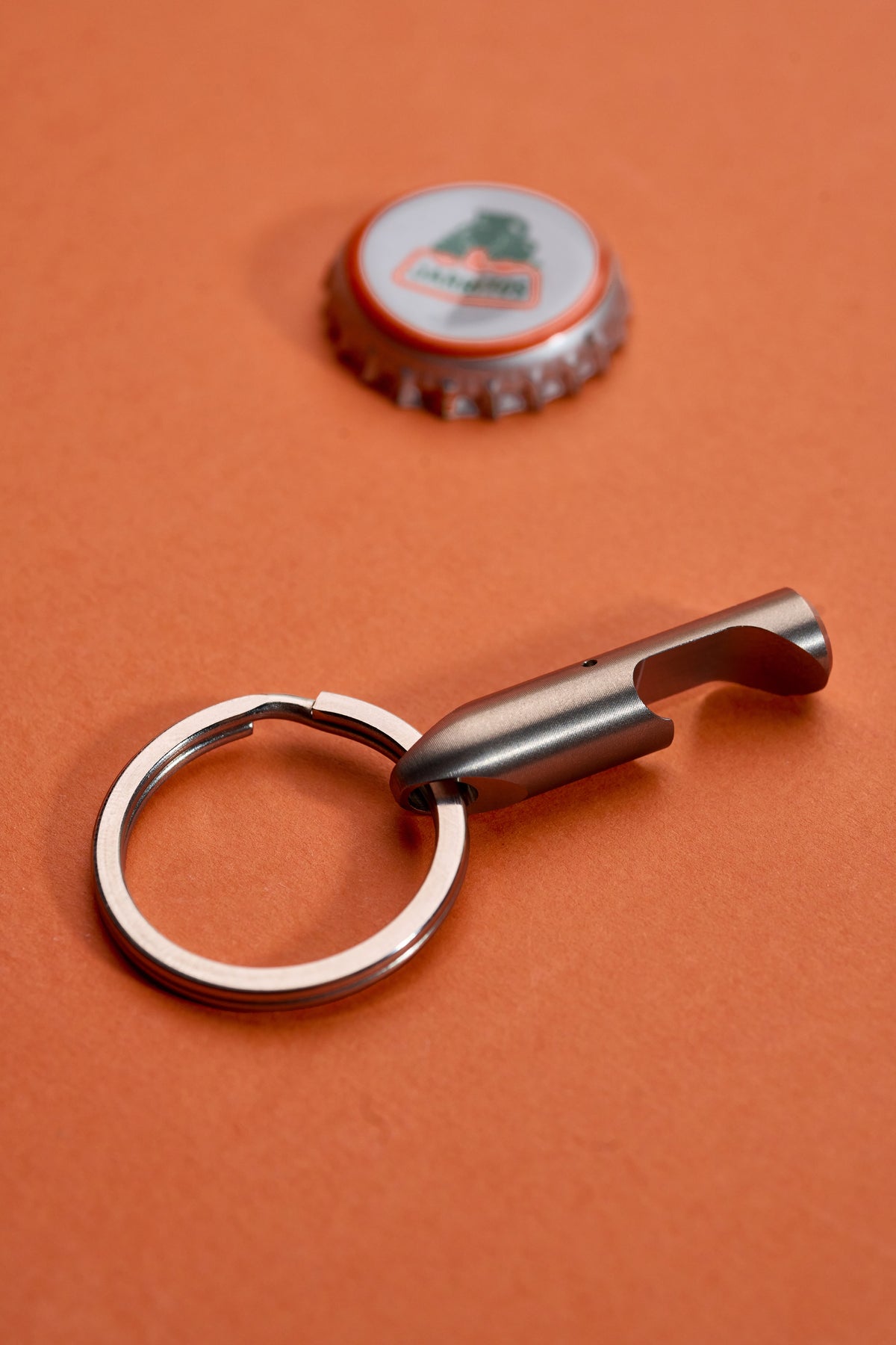 Bottle Opener - Titanium on its key ring beside a lifted cap