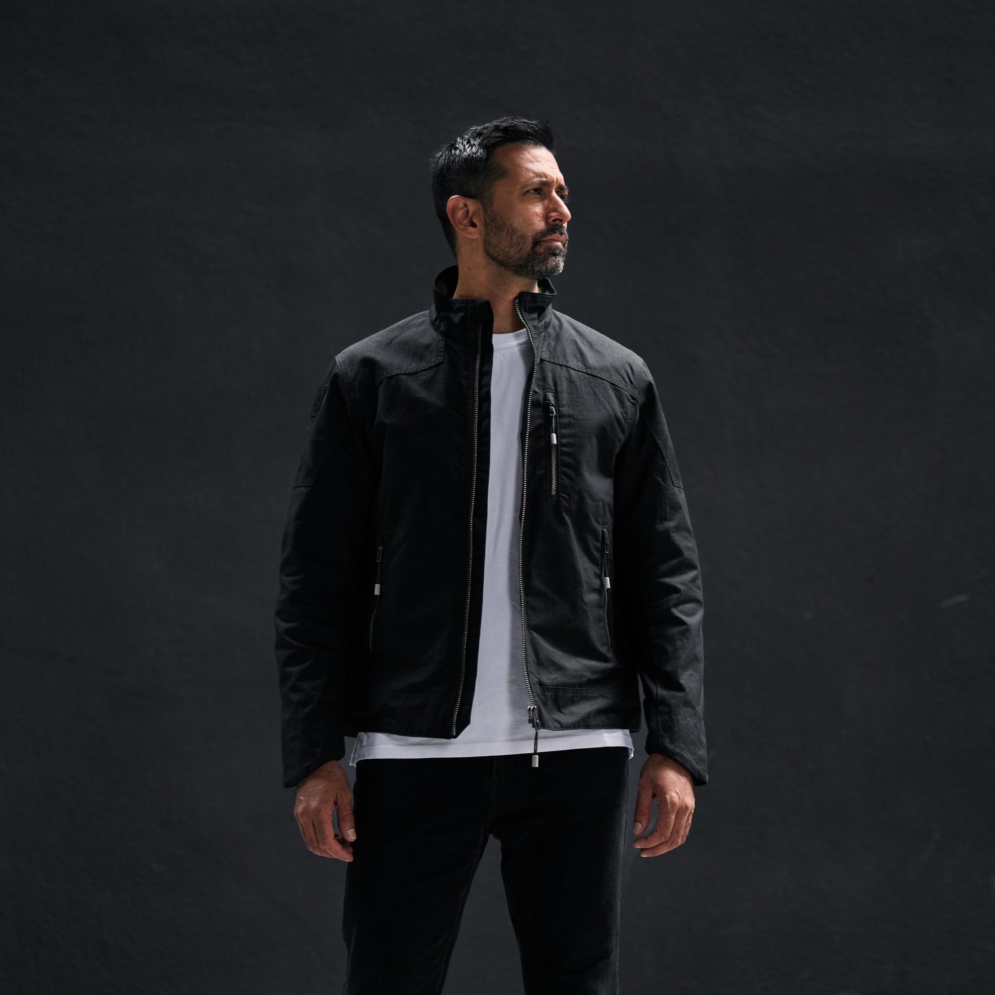 Man wearing a black jacket over a white shirt on a dark background