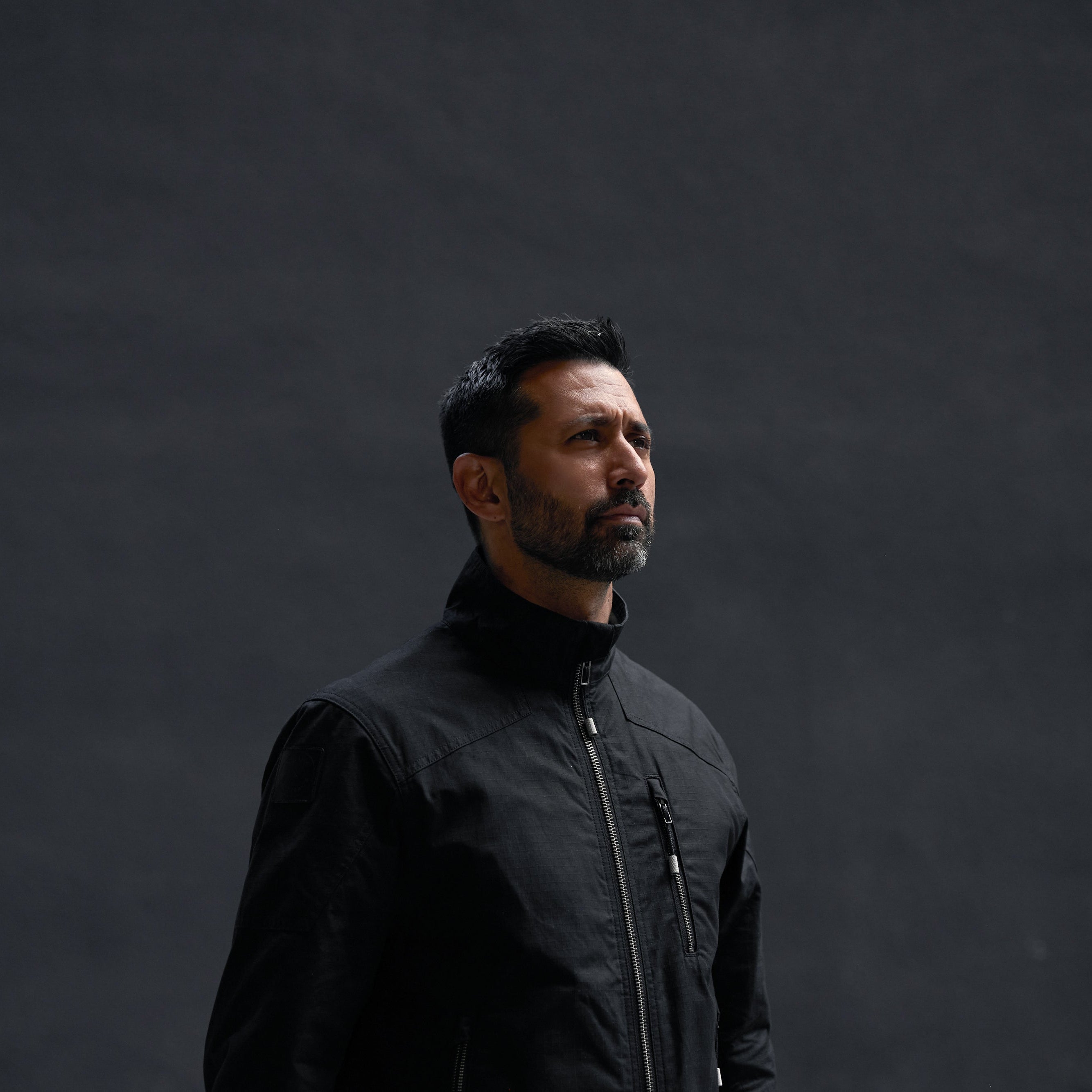 Man wearing a black jacket against a dark background