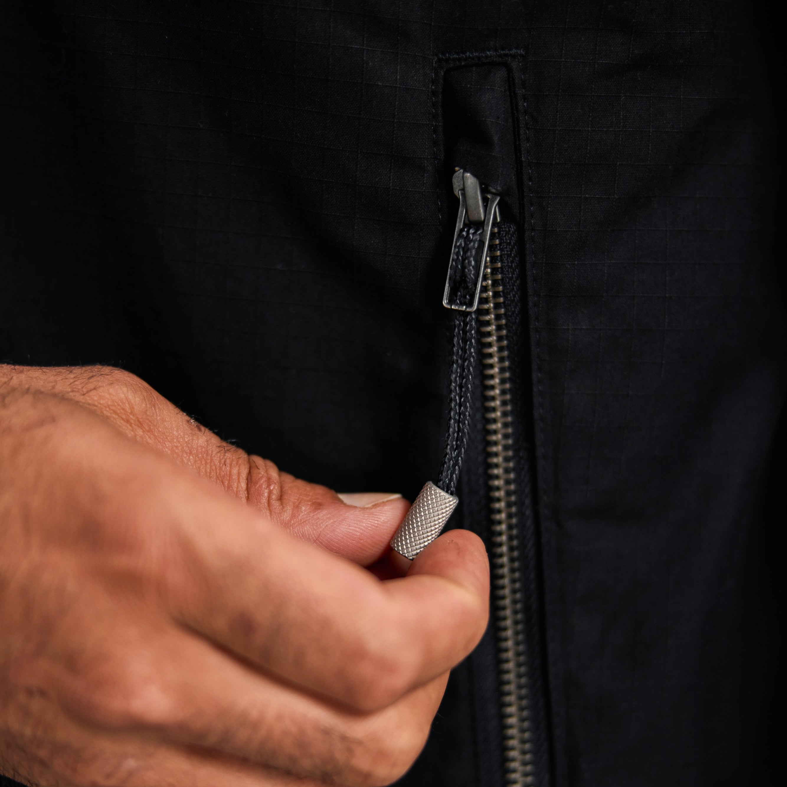 Hand zipping a black jacket with a close-up view of the zipper mechanism.