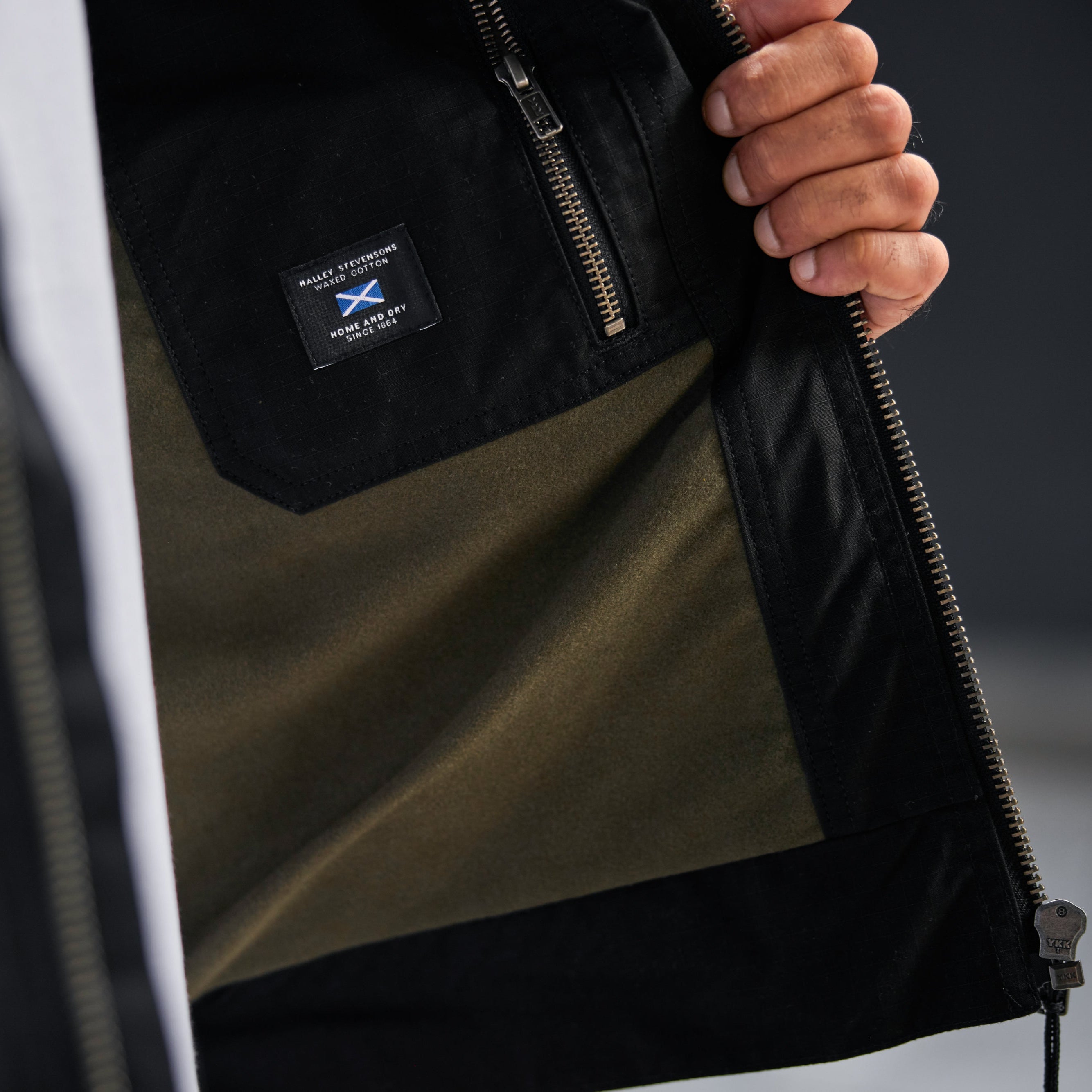 Close-up of a person holding a black jacket with a brand logo on a blurred background