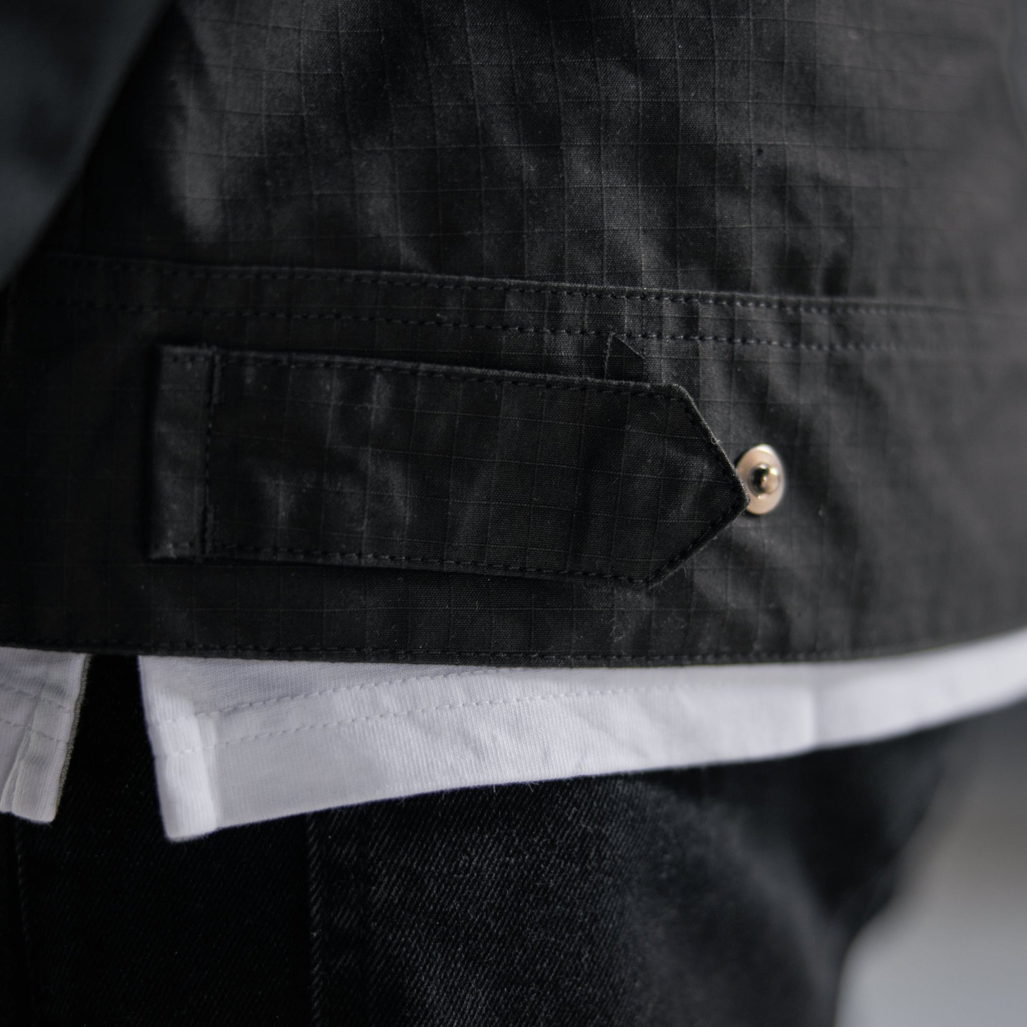 Close-up of a black jacket with a button and white shirt underneath.