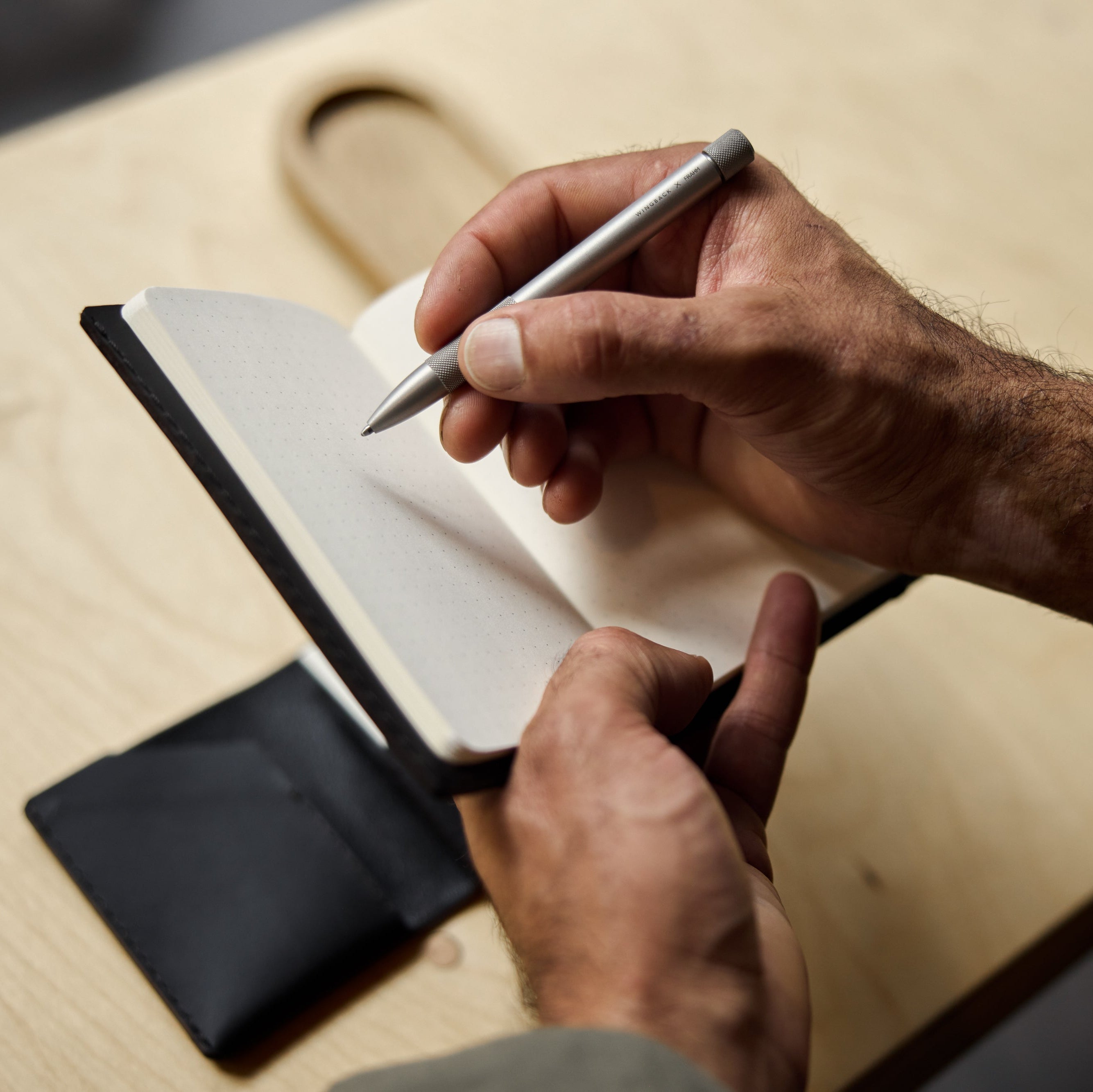 Person writing in a notebook with a pen on a wooden surface