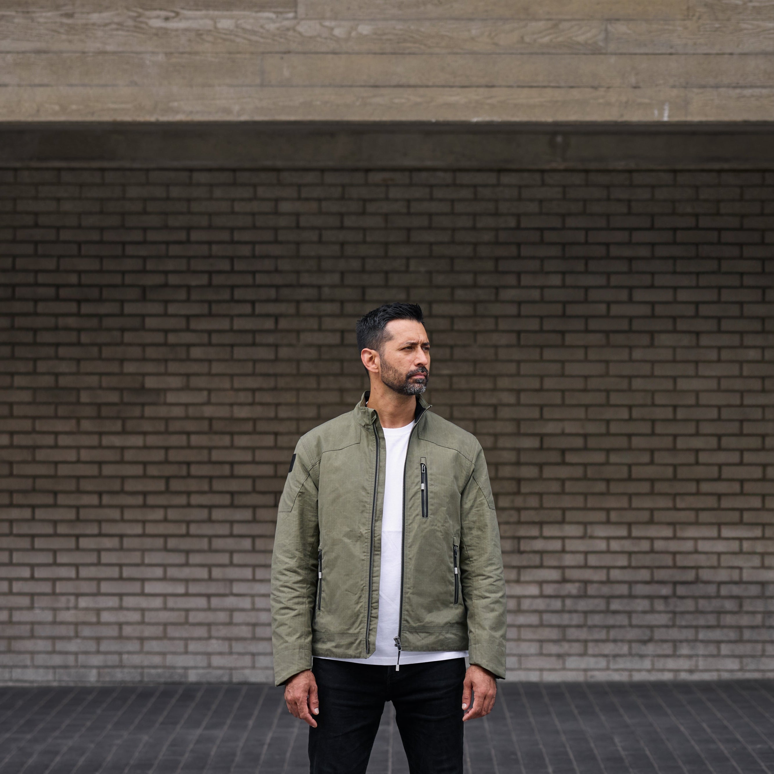 Man wearing a green jacket standing against a brick wall.
