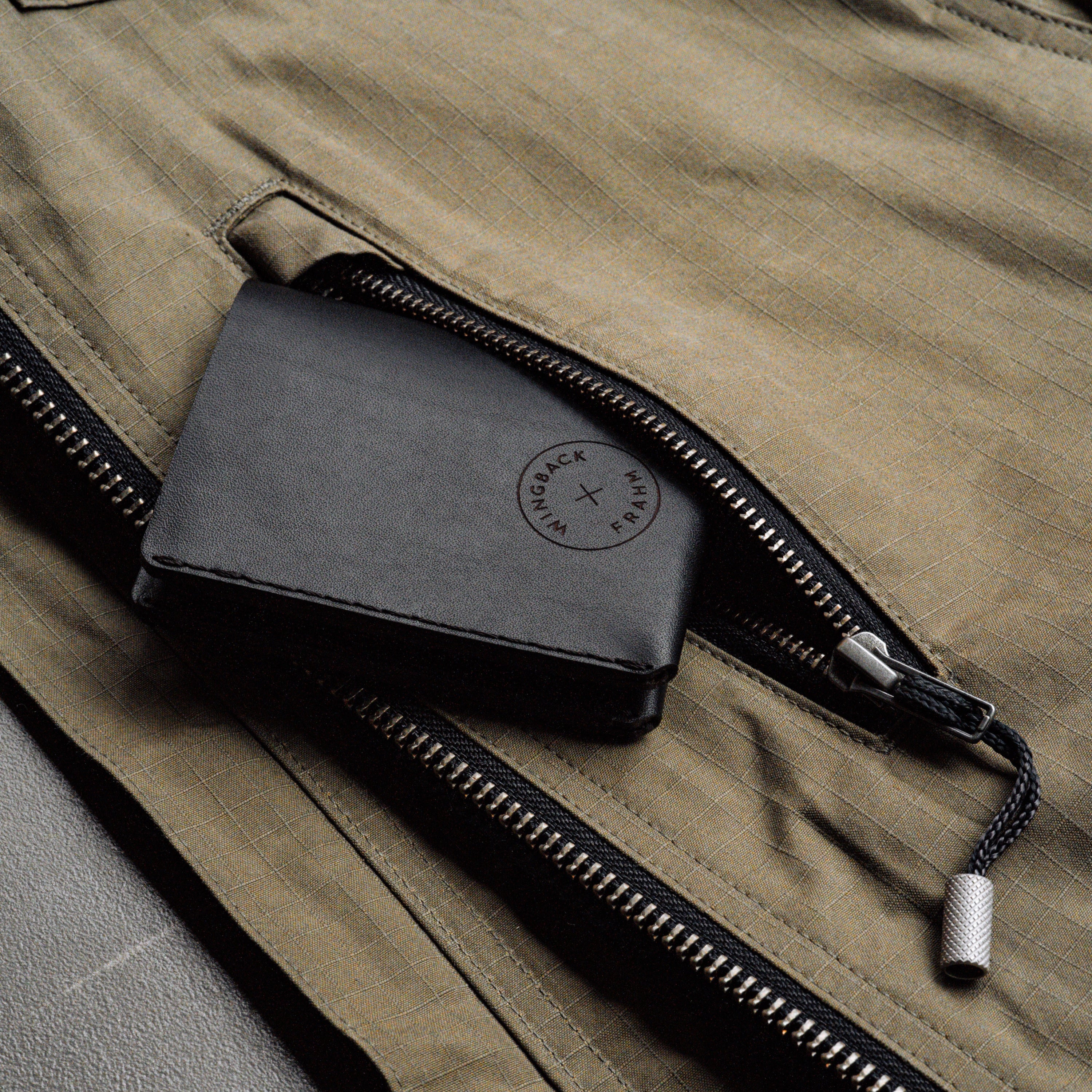 Black leather wallet with a brand logo on a brown jacket with a zipper.