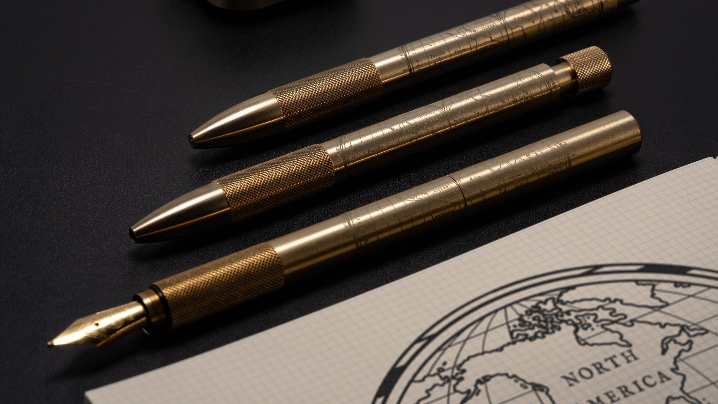 Wingback Fountain Pen, Mechanical Pen and Mechanical Pencil in machined brass beside a gridded notebook