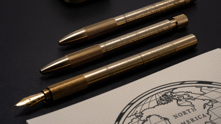 Wingback Fountain Pen, Mechanical Pen and Mechanical Pencil in machined brass beside a gridded notebook