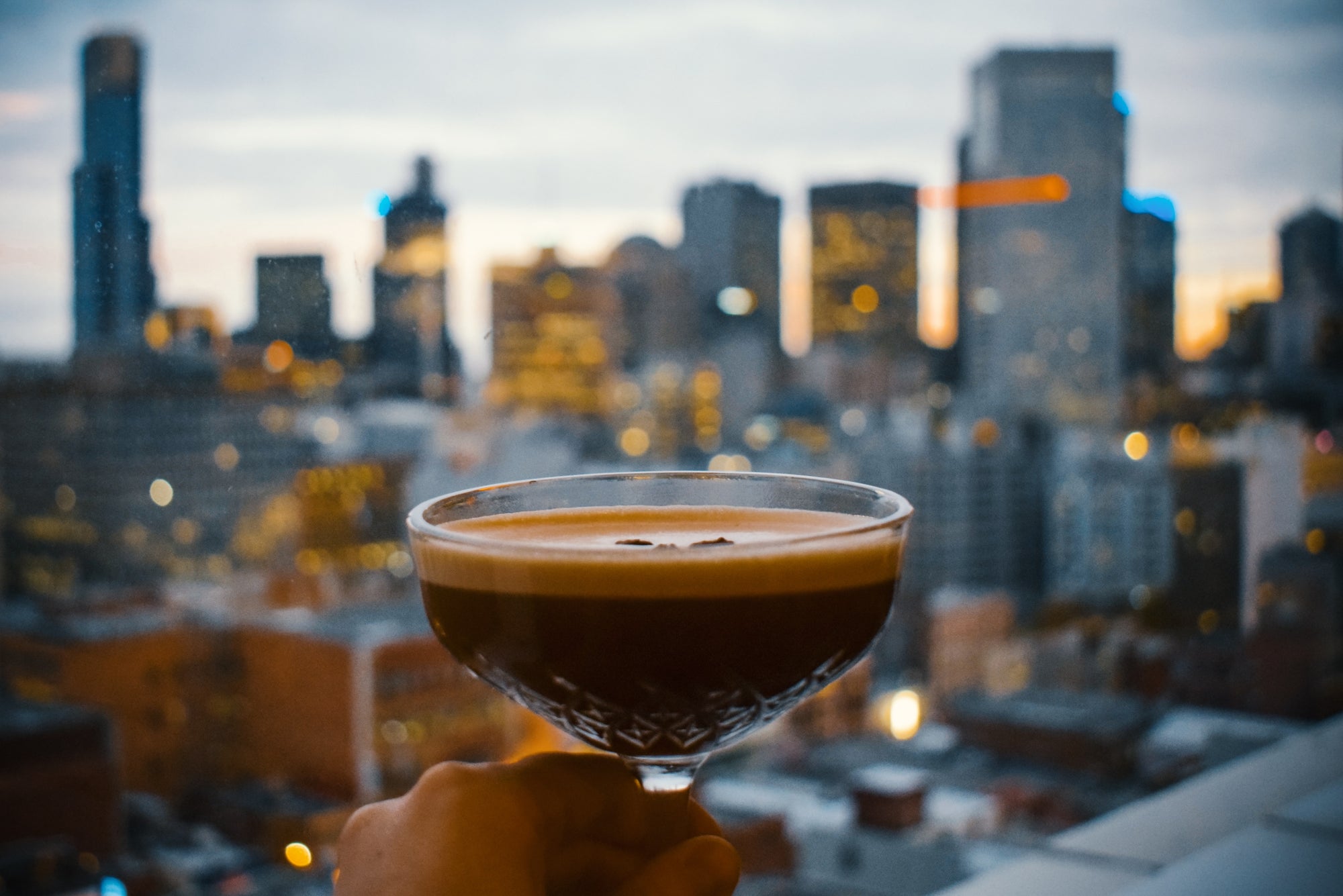 Espresso martini in foreground with a city scape in the background - Photo by Agathe on Unsplash 