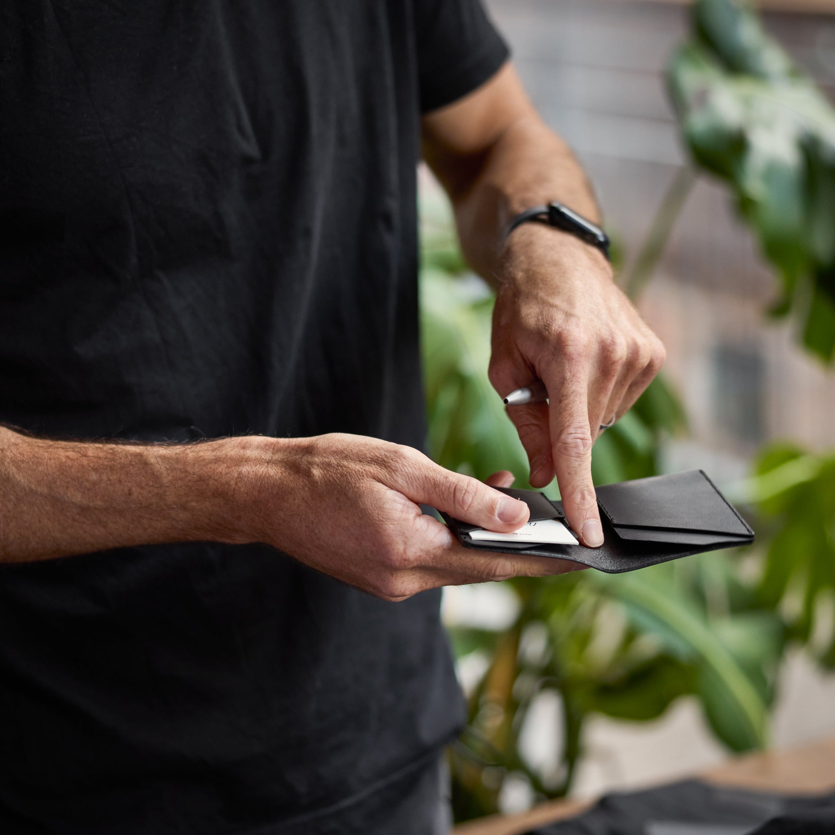 Person holding a black wallet with plants in the background